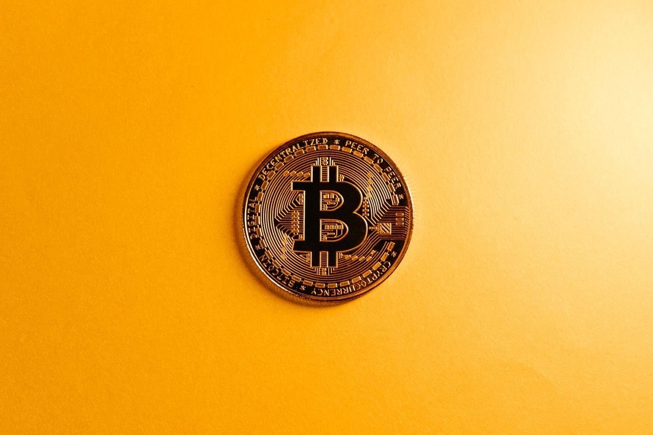Close-up of a smartphone app showing Bitcoin trading details with crypto coins on a black surface.