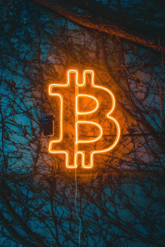 A glowing Bitcoin neon sign adds ambiance against a textured wall, ideal for cryptocurrency themes.
